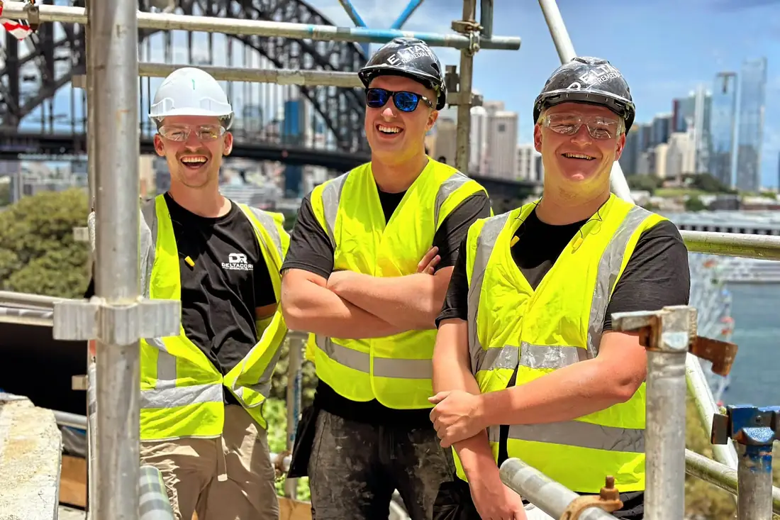 Drie vakmensen in hesjes op een steiger bij de Sydney Harbour Bridge